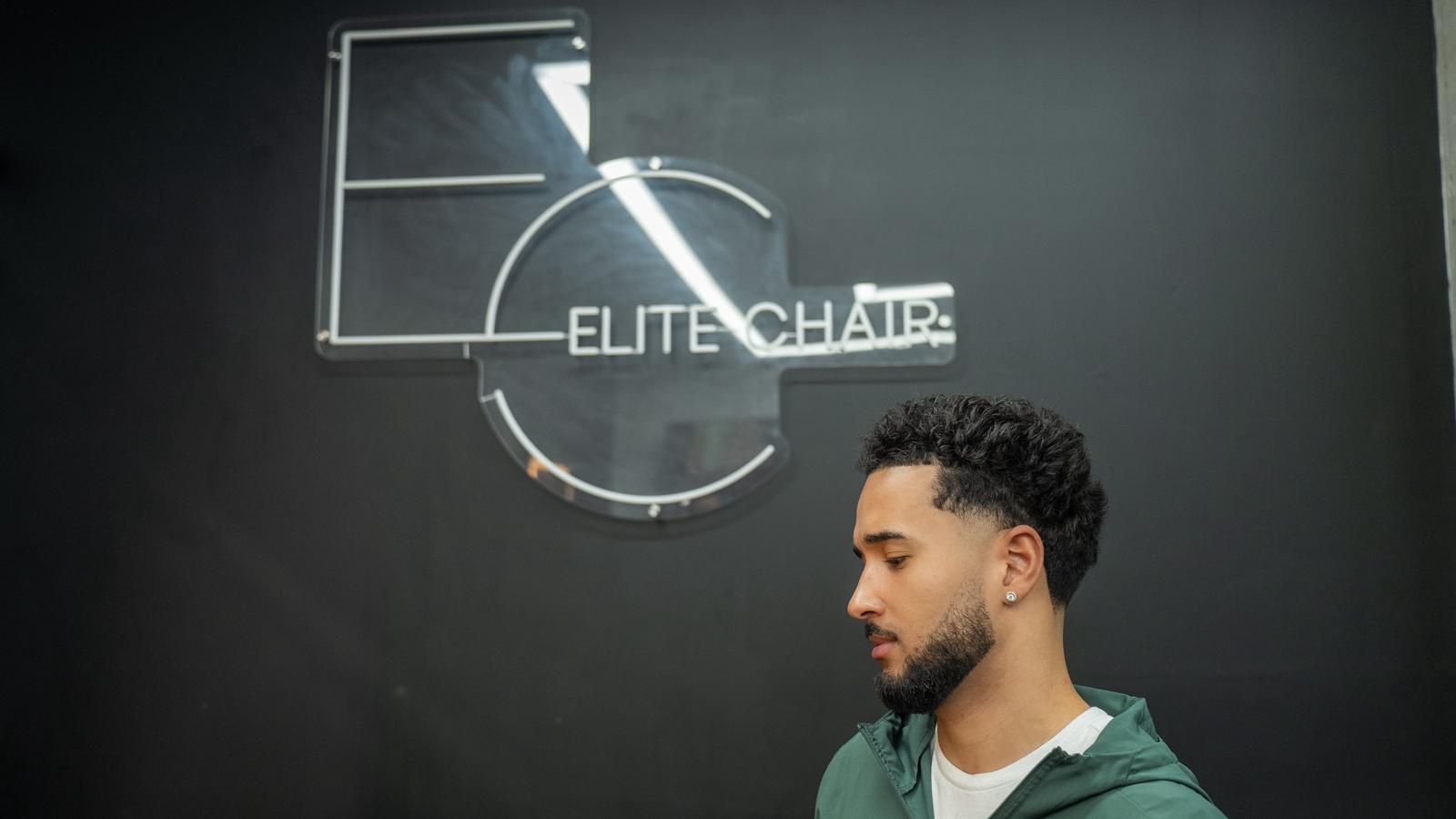 Client haircut photo in front of Elite Chair Barber logo wall