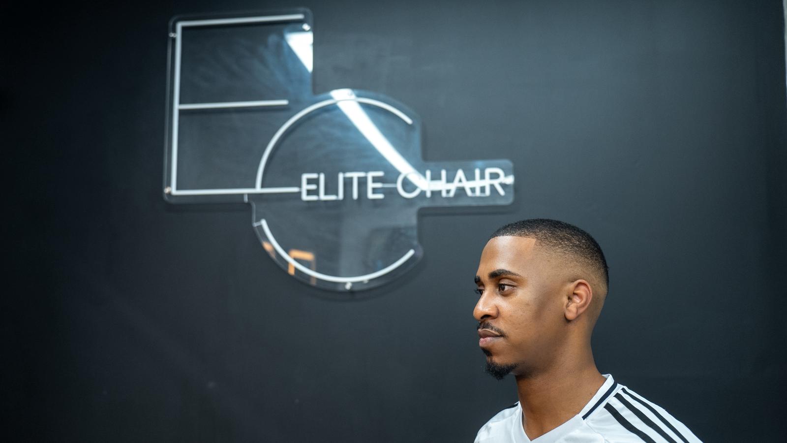 Skin fade haircut with Elite Chair Barber logo wall in Canning Town